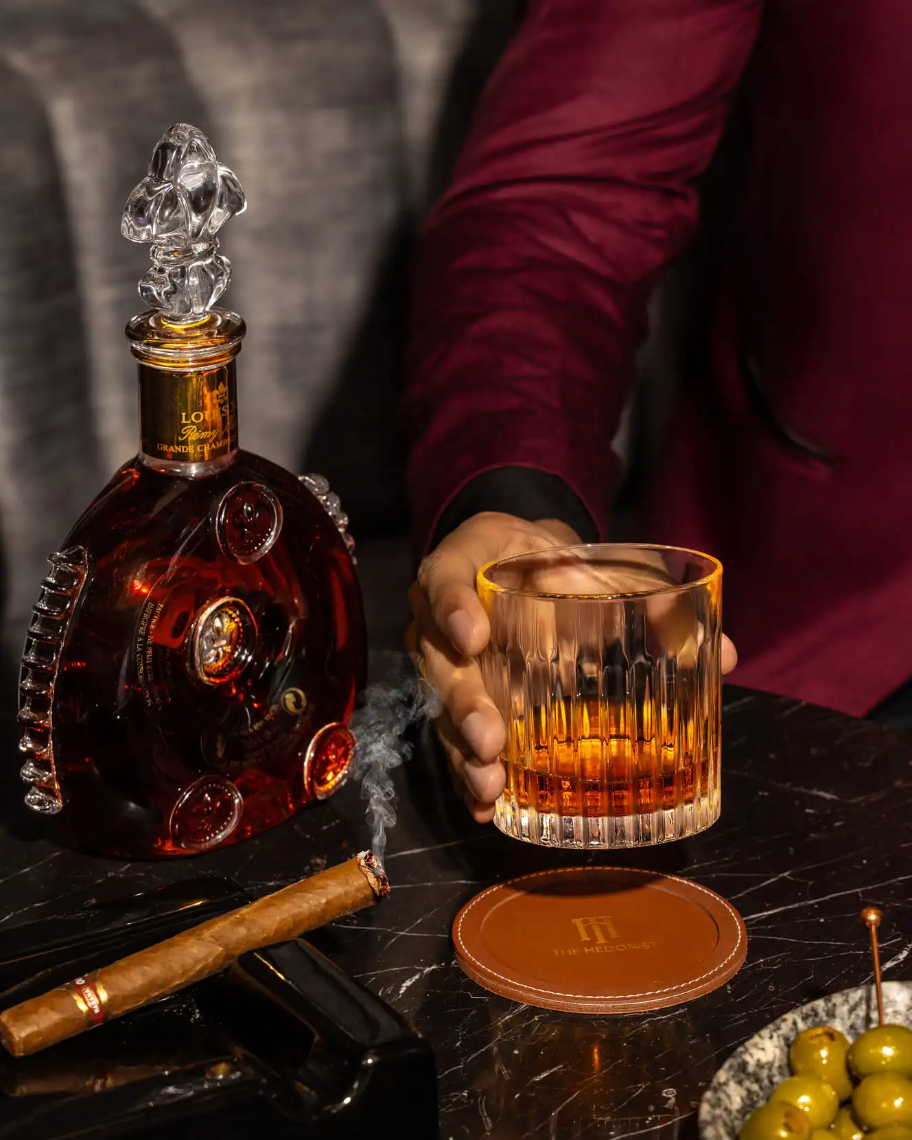 Close-up of a whisky glass, cigar, and Louis XIII bottle